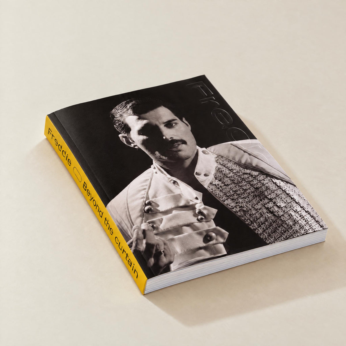 Freddie — Beyond the Curtain, softcover lying at an angle: black-and-white portrait of Freddie Mercury on the cover and a yellow spine