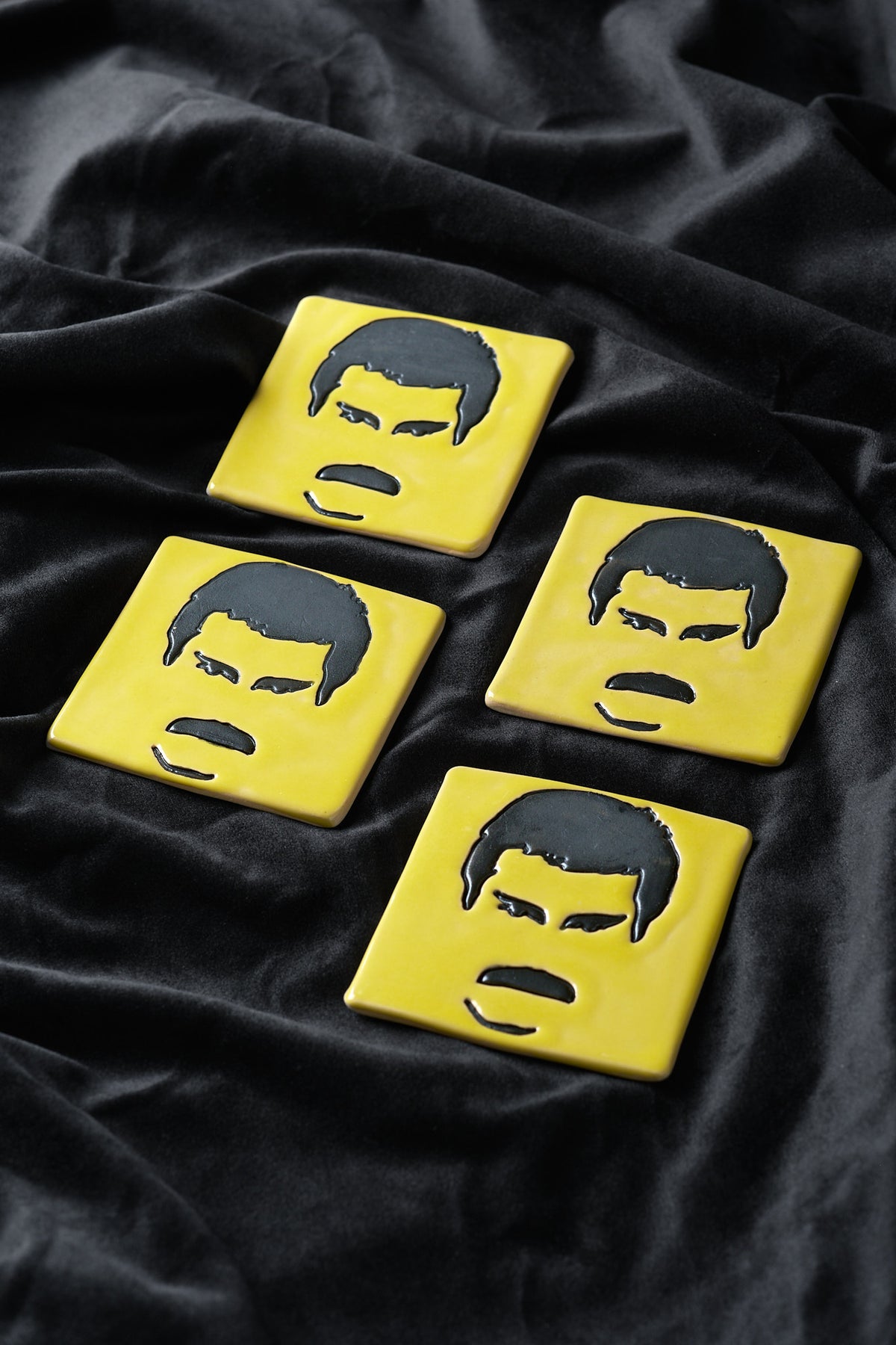 Four yellow ceramic art tiles on black velvet